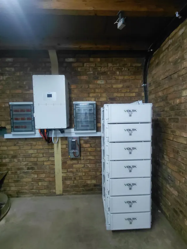 HGM Group: A commercial Deye inverter paired with a seven-module Volta HV-16 battery stack on a brick wall.